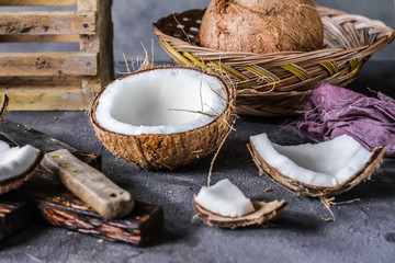 Photo of fresh coconut on a table. Tropical palm fruits. Coconut cut in half. Beach fruit. Retro dark background. Rustic wooden board. Front view. Image