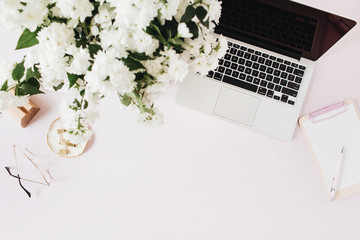 Office desk workspace with laptop, flowers bouquet and clipboard on pink table. Flat lat, top view...