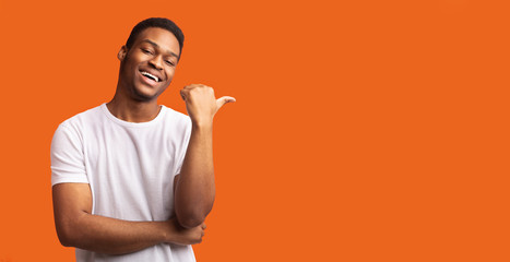 Young afro guy pointing at copy space with thumb up
