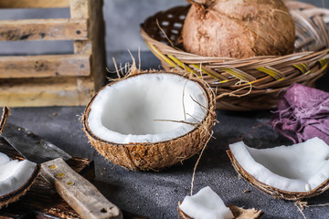 Photo of fresh coconut on a table. Tropical palm fruits. Coconut cut in half. Beach fruit. Retro dark background. Rustic wooden board. Front view. Image