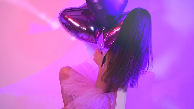Valentine Beauty model girl with colorful heart shaped air balloons laughing, celebrating holiday Birthday party. Beautiful Happy joyful romantic Young woman. Emotions. Slow motion 4K UHD