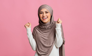 Excited middle-eastern woman celebrating success, raising hands and clenching fists