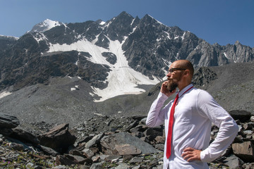 Naklejka na ściany i meble Outdoor office. Office worker in white shirt and red tie talking on the phone in alpine landscape.