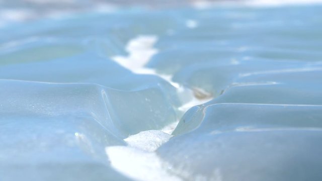 MACRO, DOF: Detailed shot of frozen Lake Abraham glimmering in the winter sunshine. Beautiful turquoise water freezes over a lake in Jasper National Park. Crystallized snow gathers in frozen grooves.