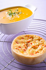 A small quiche with a bowl of soup on the background. On top of a grill grid in a purple tablecloth.