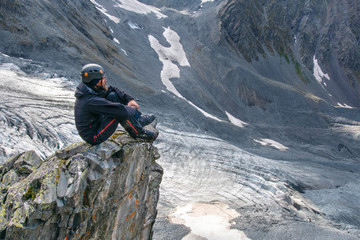 A mountain climber (hiker) sits on the cliff edge above glacier.