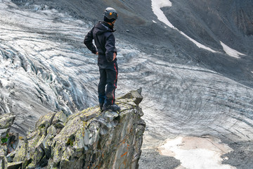 A mountain climber (hiker) stands on the cliff edge above glacier.