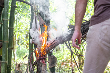 Obraz premium Man is roasting chicken with with dry coconut leaves bonfire at camping in the forest.
