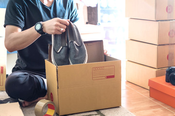 Thai young male online seller and start up small business owner putting shoes into a box and...