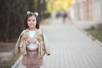 Smiling child girl 3-4 year old walking on street wearing spring clothes outdoors. Looking at camera. Childhood.