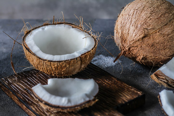 Photo of fresh coconut on a table. Tropical palm fruits. Coconut cut in half. Beach fruit. Retro dark background. Rustic wooden board. Front view. Image