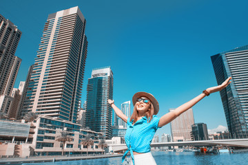 A happy tourist girl holds up her hands and enjoys the stunning view of the skyscrapers in the Dubai Marina area. Travel to the United Arab Emirates