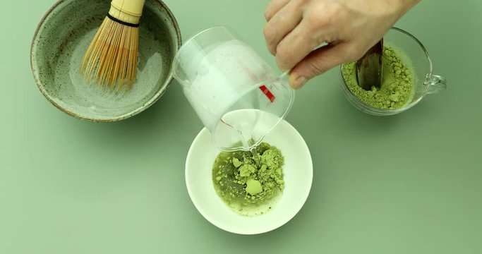 Blending green matcha tea powder in hot water with bamboo whisk to make green matcha tea latte