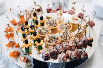 canapes with bacon, olives, cheese, cucumber and red fish on a plate