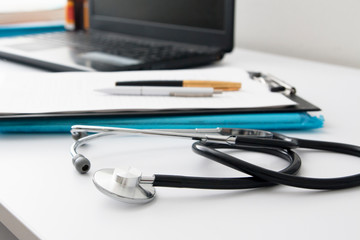 Doctor's workplace: close up stethoscope, defocused laptop, documents, pens. Medical concept