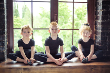 Portrait of 3 little children dancer two girls and one boy in black leotard sitting on window at...