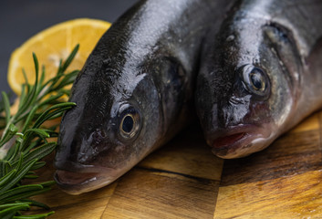 fresh sea bass with rosemary and lemon on a wooden board, two fish