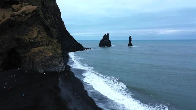 4K Drone Shot Rising Over The Black Sand Beach In Iceland, Violent Waves Over-Cast. Famous Black Sand Beach In Iceland South Of Iceland, Cloudy Day. Next To Big Rock Cliffs