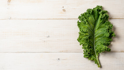 Fresh green kale leaf on white wooden tabletop, copy space left. Flat lay or top view. Healthy detox vegetables. Clean eating and dieting concept. Health kale benefits. Banner - obrazy, fototapety, plakaty