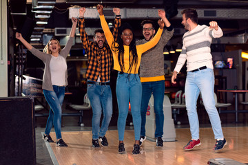 Group of friends enjoying time together laughing and cheering while bowling at club.