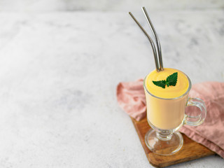 Yellow mango yogurt or smoothie on gray cement background with copy space left. Turmeric Lassie or lassi in glass with metal straws