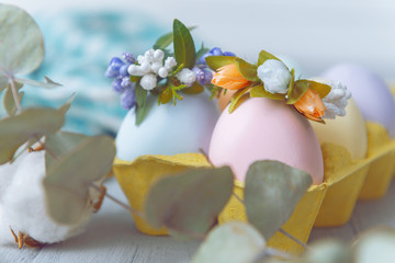 Easter concept. Easter eggs painted in pastel colors in an egg tray with wreaths on them. Light background, place for text.