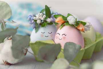 Easter concept. Easter eggs painted in pastel colors with cute faces in an egg tray with wreaths...