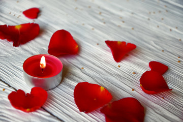 Red rose petals and red burning candle on a white wooden background. St. Valentine's Day background. 