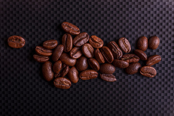 Roasted brown coffee beans on black carbon table or dark background.