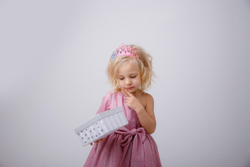 cute little girl in a princess dress with a crown holding a gift on a white background
