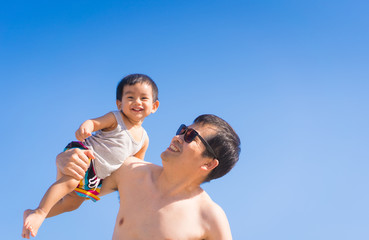 Asian father is playing and holding his happy little baby boy on the backgroud of blue sky in...