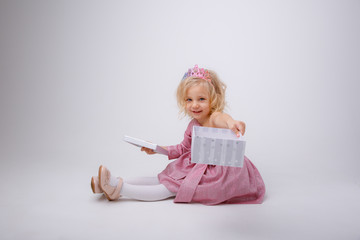 a blonde girl with a gift in a Princess dress sits on a white background