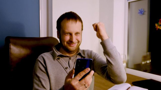 Happy man holding smartphone and celebrating his success indoors. 