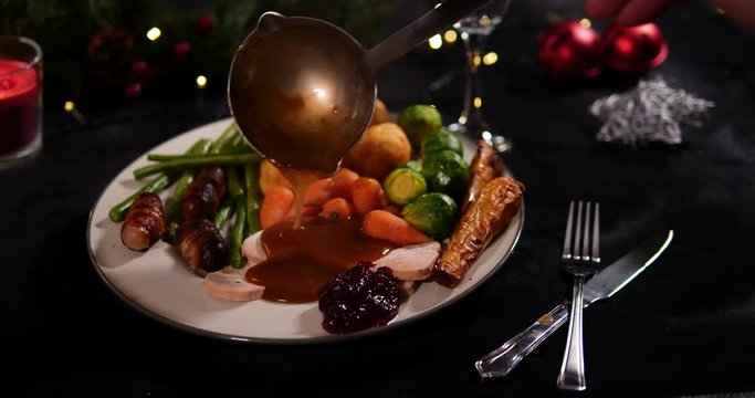 Pouring Gravy on Christmas dinner plate for a festive meal. A ladel is used to pour onto the Roast Turkey and vegetables