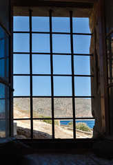 view from an old building through a window with metal bars on the mountains and the sea, Greece