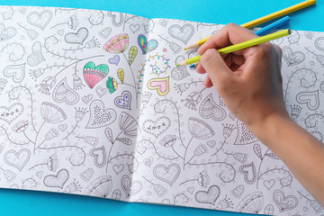 Female hands coloring anti stresss color book with hearts and flowers pattern. Art therapy concept. Healthy lifestyle, leisure. Artwork for adults.