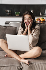 Image of young beautiful woman using laptop computer on sofa at home