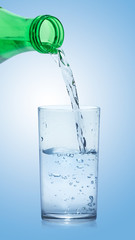 Pouring pure clear water from bottle into glass on blue background.