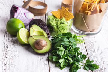 Mexican traditional food, guacamole sauce ingredients  avocado, red onion, cilantro, lime and tortilla corn chips