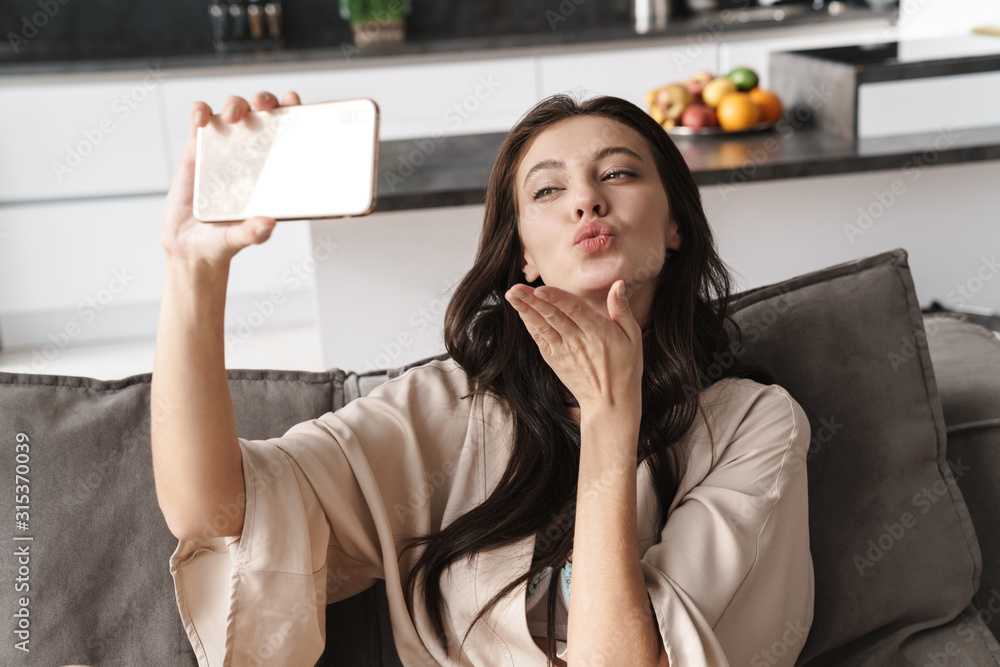 Poster Image of young beautiful woman taking selfie photo on cellphone at home