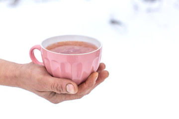 Hand holds a pink mug with a drink on a background of a winter landscape