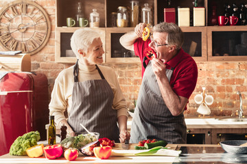 Cheerful senior man amusing his wife preparing lunch at kitchen
