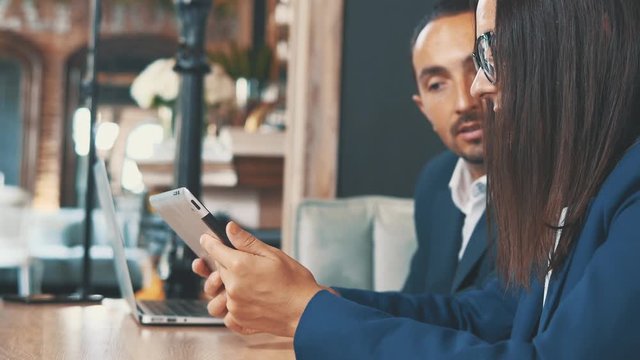 Two businesspeople in deep blue suits are working on laptop and tablet, sitting in coffee shop. Side view. Crop. Close up. Copy space.