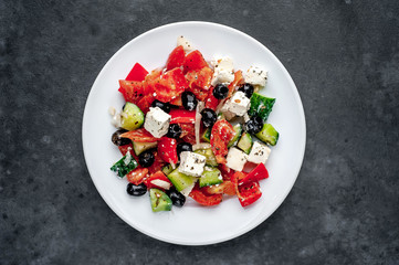 Greek salad in a white plate on a stone background