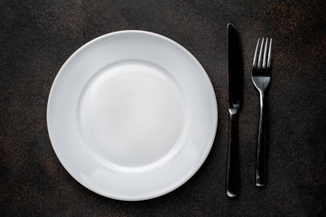 white plate with  fork and knife on a stone background
