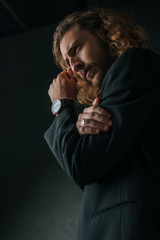 Fototapeta na wymiar low angle view of tense fashionable businessman in black suit posing in dark