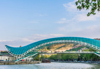 The view on the Peace Bridge with the Sololaki Hill and old town buildings on the background, Tbilisi, Georgia.
