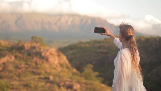 Woman Taking Pictures of Mountain Landscape. Girl is Taking photos with smartphone of summer hills landscape at sunset