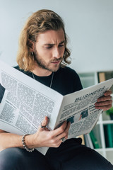 Naklejka premium fashionable casual businessman in total black outfit reading business newspaper in office