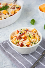 Close up rise salad in a white bowl with melon, stick of ham and vegetable.